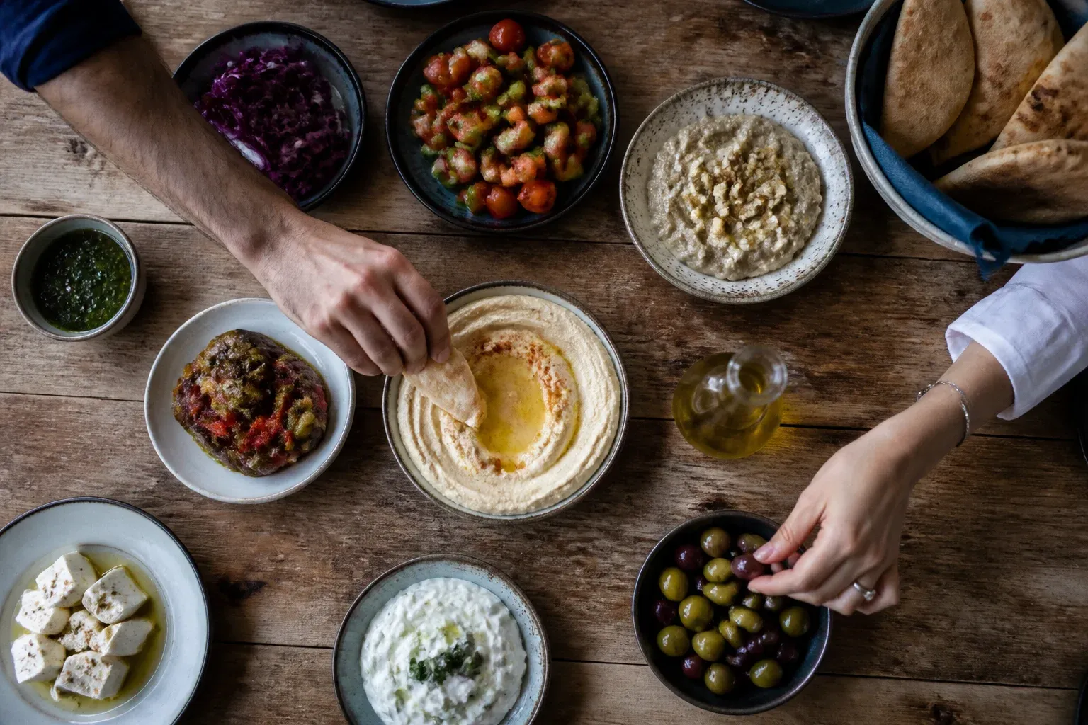 שולחן עץ מלא בצלחות מזה, פיתה ושמן זית, מצולם מלמעלה