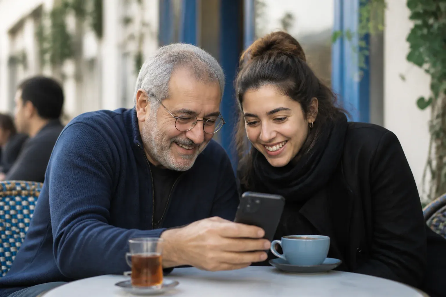 שני שכנים בבית קפה מביטים יחד בטלפון וצוחקים